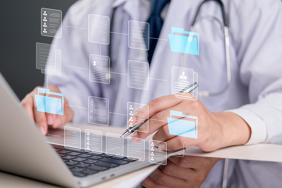 A doctor with a stethoscope around his neck sits before a laptop with diagrams projected from the display